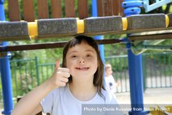 Young child giving a thumbs up outdoors on a playground 5kGwA5