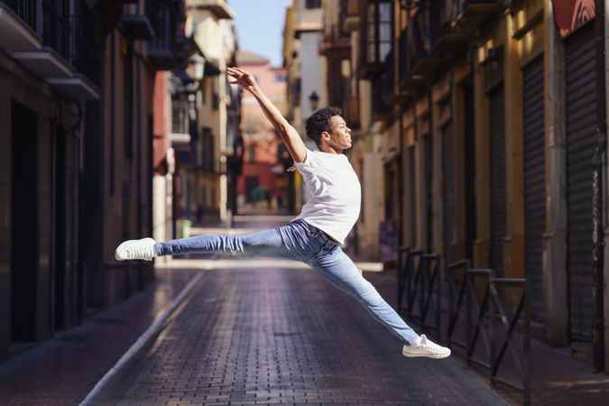 Male dancer in jeans and t-shirt leaping on an empty European street
