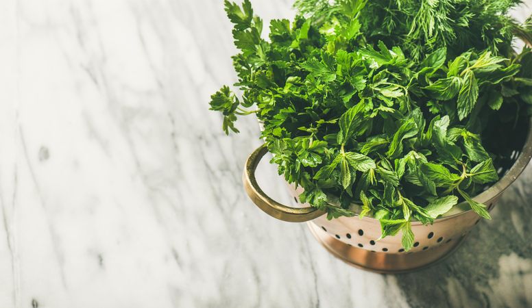 Top view of colander full of fresh green herbs, horizontal composition, copy space