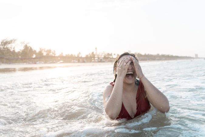 A young Hispanic woman is laughing playing with the waves in the sea at the beach