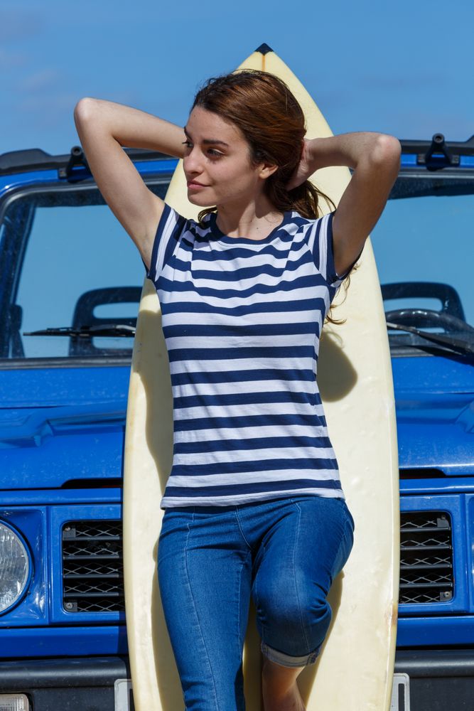 Woman leaning on big surfboard near car
