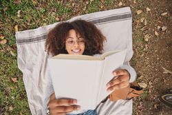 Positive Black Latina female reading book in park