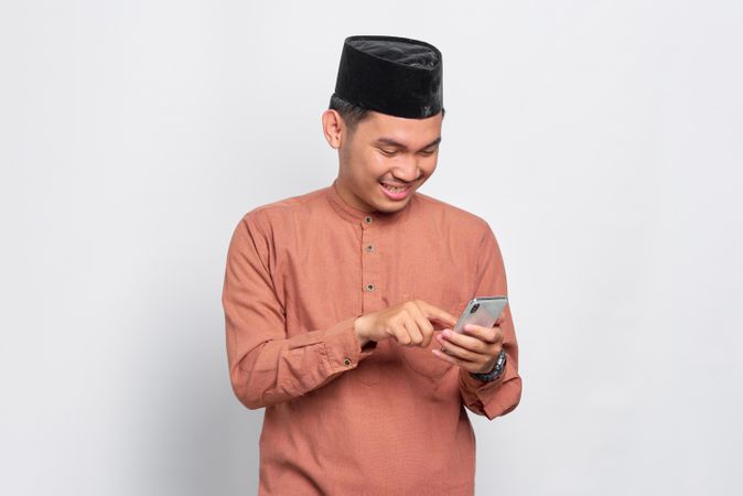 Muslim man in kufi hat smiling and looking down at mobile phone