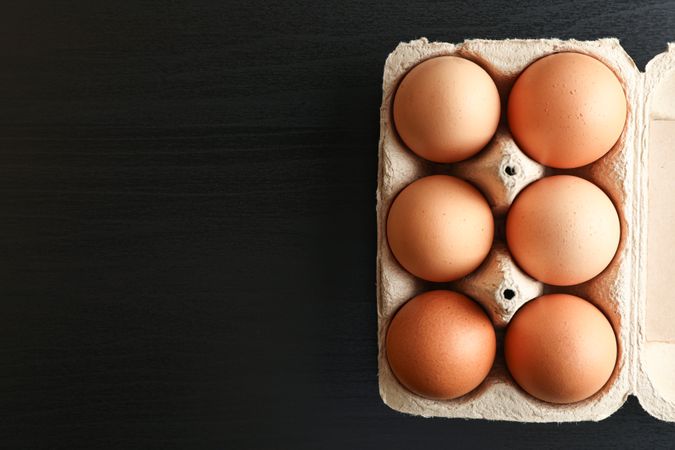 Brown chicken eggs in carton box on dark background, space for text and top view