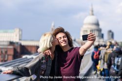 Blonde female and curly haired boyfriend taking picture with cell phone on bridge in London 0veWZb