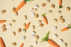 Easter eggs and carrots on pastel yellow background