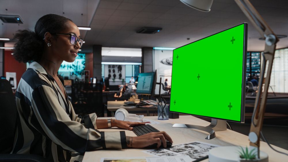 Portrait of Creative Black Female Sitting at a Desk Using Desktop Computer with Mock-up Green Screen.