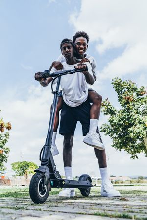 Black man riding on electric scooter in park with friend on back