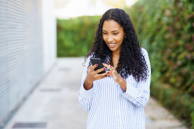 A young woman happily engaged with her smartphone while enjoying an outdoor setting nearby