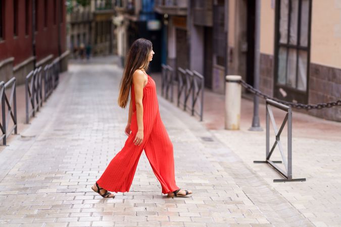 A stylish woman in a vibrant red dress is gracefully walking through an urban street