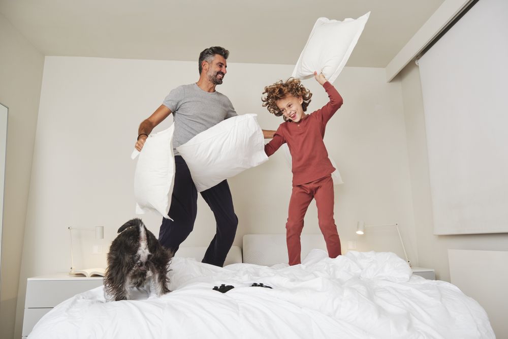 Cheerful man and boy jumping on bed together