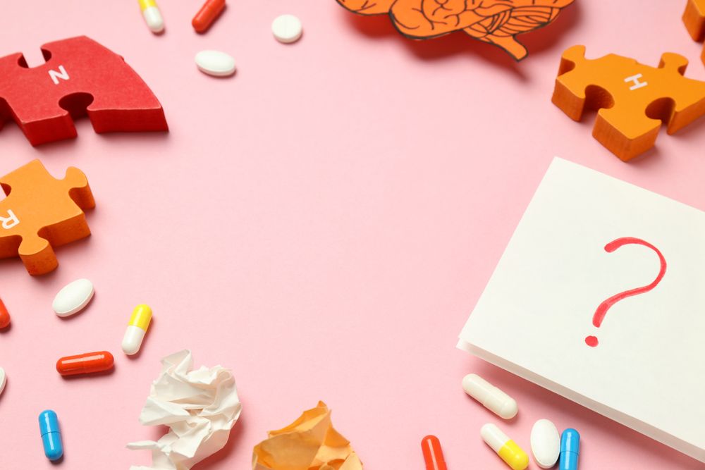 Pink paper framed with pills, puzzle pieces, brain and question mark with copy space