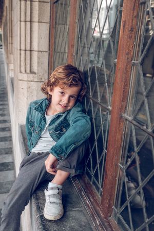 Charming boy sitting near window outside