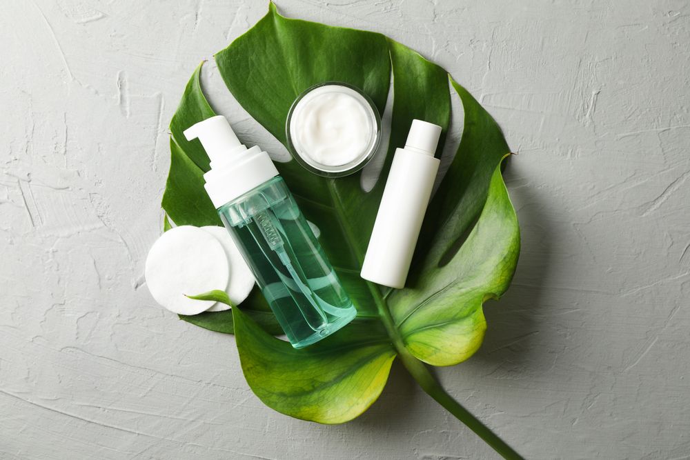 Flat lay with body care accessories and palm leaf on grey background, copy space