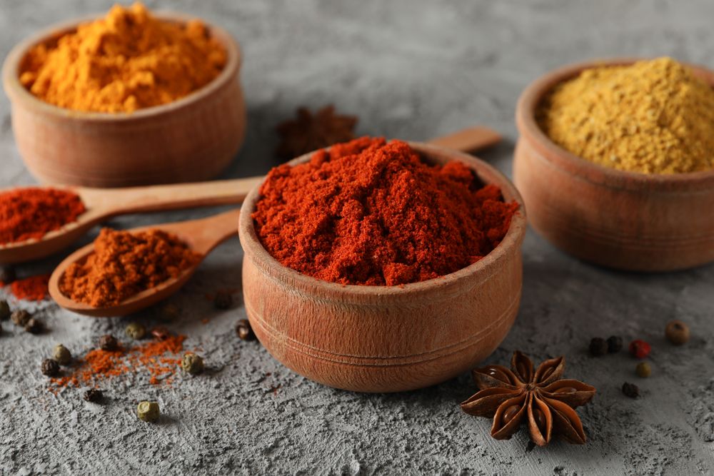 Side view of wooden bowls with red, yellow and brown spices