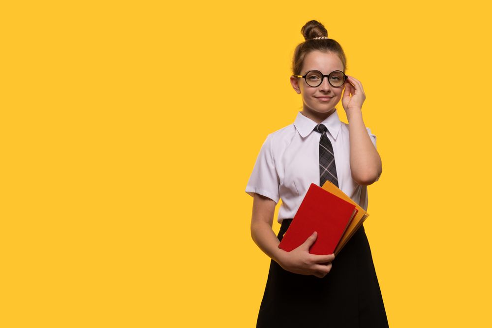 Teen girl adjusting glasses, holding books, wearing school uniform