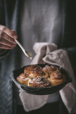 Crop woman adding sauce to cinnamon rolls