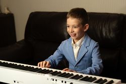 Cheerful young boy in blue blazer playing the piano.
