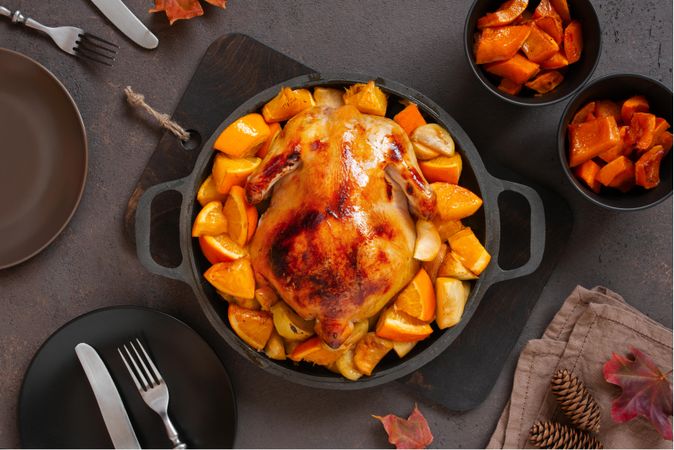 Chicken roasted in pot with oranges on table