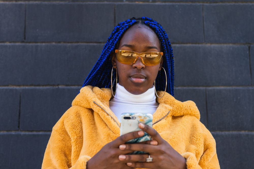 woman in trendy outfit browsing cellphone in city