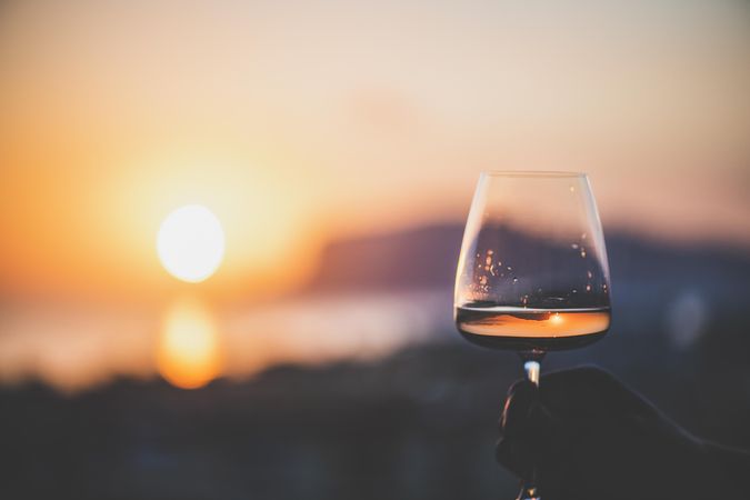 Man's hand holding glass of rose wine against sunset, horizontal composition