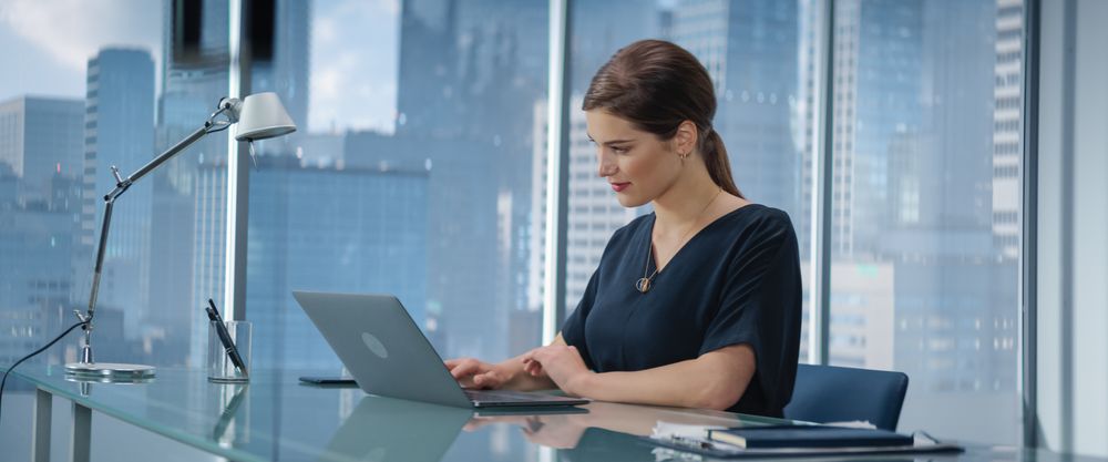 Portrait of Young Successful Businesswoman Sitting at Desk Working on Laptop Computer in City Office.