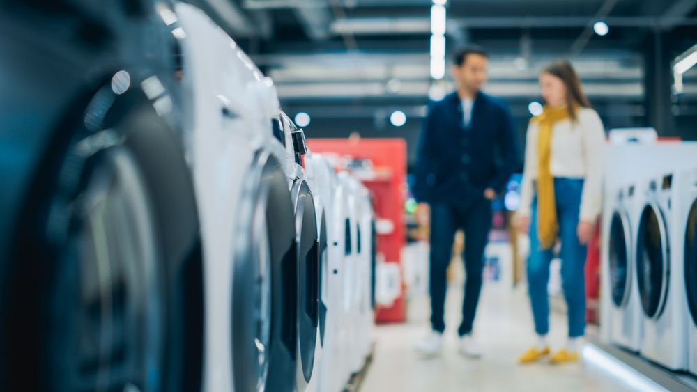 Multicultural Couple Evaluates Washing Machine Choices at Home Electronics Store.