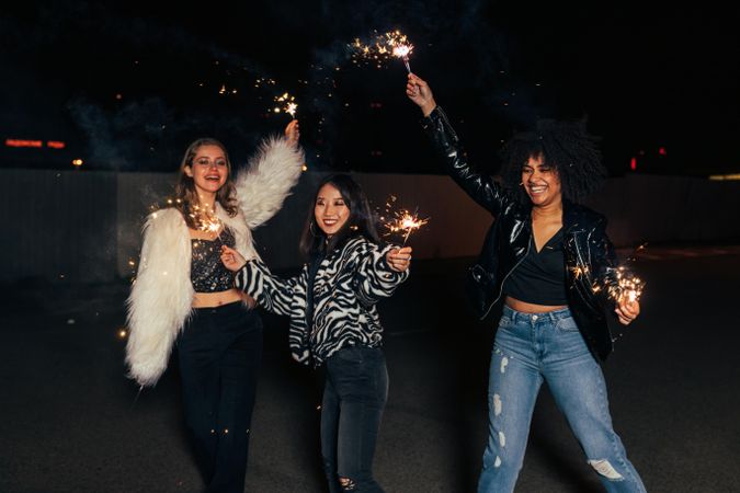 Three women laughing together with sparklers at night