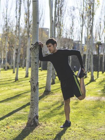 man leaning against a tree stretching his quadriceps.