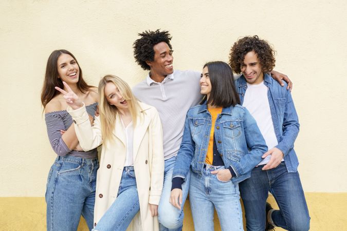 Smiling friends posing for portrait leaning against a yellow wall