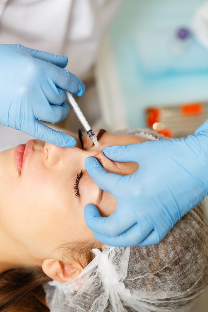 Hands in latex gloves injecting botox into wrinkles of female client