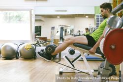 Muscular male in green t-shirt working out using leg extension machine 5oL2z4