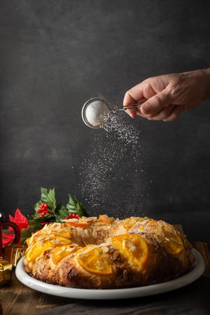 Person dusting powdered sugar over an orange cake