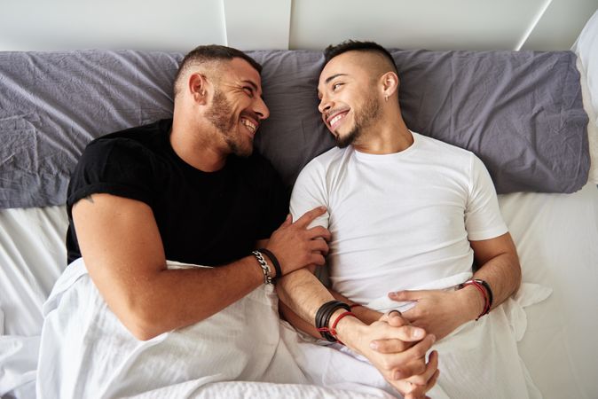Smiling gay couple hugging on bed