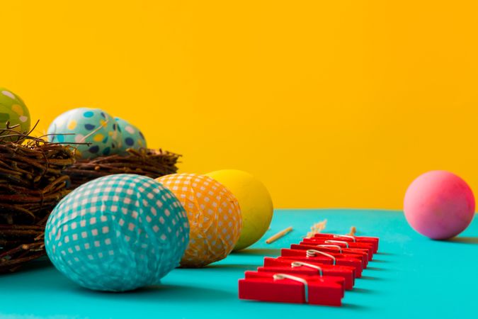 Side view of right Easter eggs, birds nests and clothes pins on cyan paper