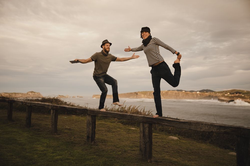 Couple holding hands and jumping on bench on shore near water