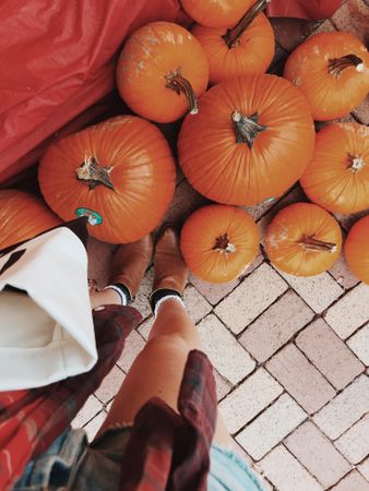 Cropped image of a woman standing in front of pile of orange pumpkins