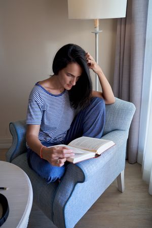 Hispanic woman reading book in armchair