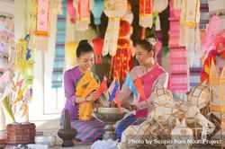 Two women in their traditional Thai outfit sitting on floor surrounded by decoration 48Qkvb
