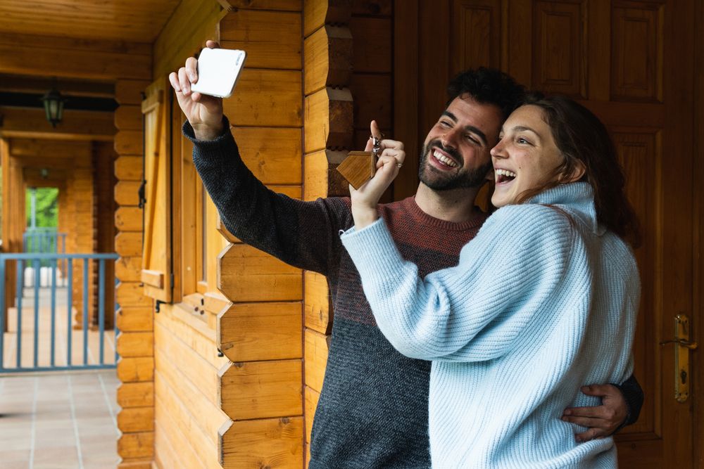 Delighted couple with keys of new house taking selfie on terrace