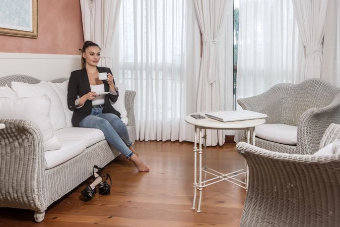 Woman in blazer drinking coffee and sitting on couch