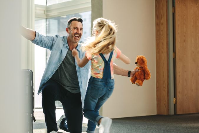 Girl running towards her father at the entrance door holding a teddy bear