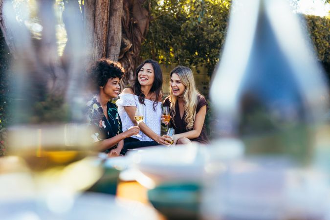 Three young women sitting outdoors with glass of wine and smiling