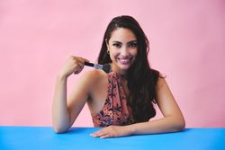 Happy Hispanic woman with long brown hair holding up large make up brush and smiling at camera