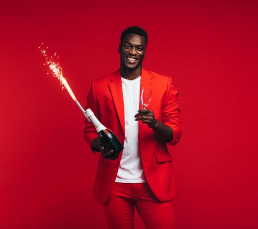 Handsome man with champagne bottle, glass and firework in hand