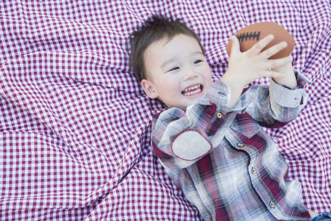 Young Biracial Boy Playing with Football on Picnic Blanket