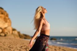 Woman stretching her arms facing the ocean on beach at sunset