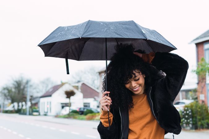 Smiling Black woman with umbrella on street