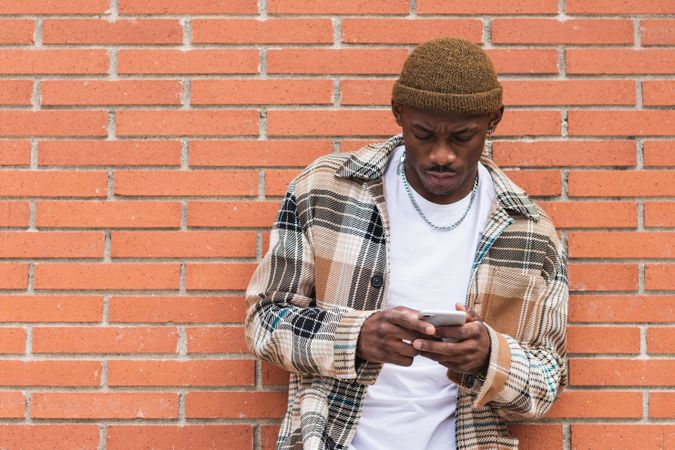 Black man using smartphone near brick wall