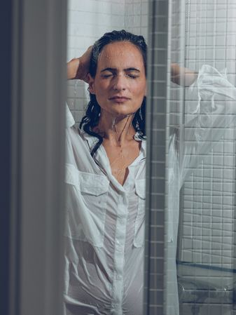 female in wet shirt touching head in shower cabin